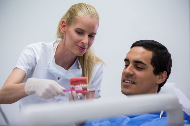 Dentista explicando a un paciente con un modelo dental cómo cuidar sus implantes